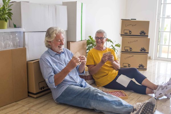 Happy couple of senior people sitting in the floor having a break with food and drink in the new home for new beginning like retired with moving boxes on the floor