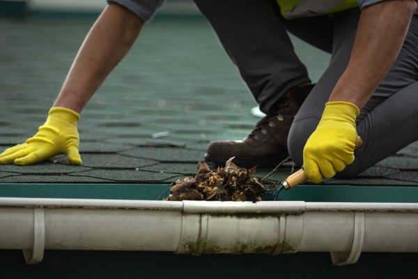 A man worker is cleaning a clogged roof gutter from dirt,