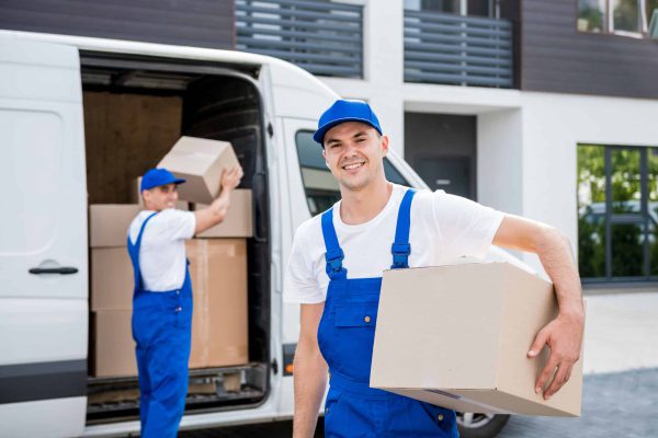 Two removal company workers unloading boxes from minibus into new home.